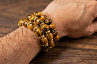Bracelet homme en œil du tigre sur-mesure posé sur une surface en bois sombre, avec des perles dorées intercalaires et des détails artisanaux