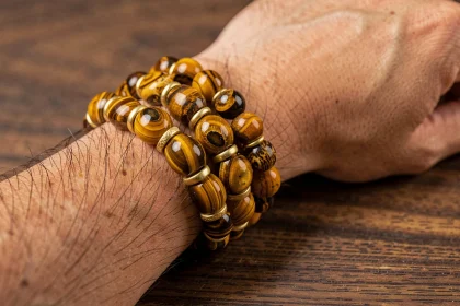 Bracelet homme en œil du tigre sur-mesure posé sur une surface en bois sombre, avec des perles dorées intercalaires et des détails artisanaux